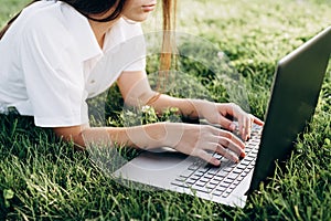 Student girl with laptop outdoors. woman lying on the grass with a computer, surfing the Internet or preparing for exams.