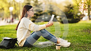 Student girl reading book in park, sitting on grass