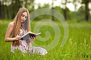 Student girl sit on lawn and reads textbook.