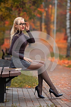 Student girl sitting on the bench in the autumn park.