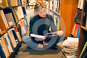Student girl sitting on the floor and reading a book in the library