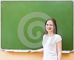 Student girl standing near clean blackboard in the classroom