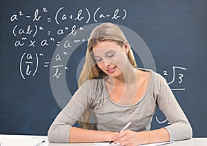 Student girl at table writing against blue blackboard with education and school graphics