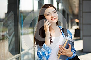 Student girl talking on mobile phone standing near college build