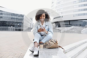 Student girl using smartphone in a city. Smiling woman looking at mobile phone outdoors.