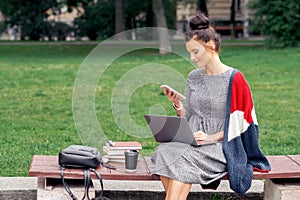 Student girl is using a smartphone while sitting on a wooden bench.