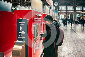 Student girl in winter clothes pays for train fare in red vending machines in the main hall of the Copenhagen Central