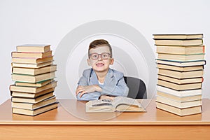 A student with glasses sits at a table with books on both sides