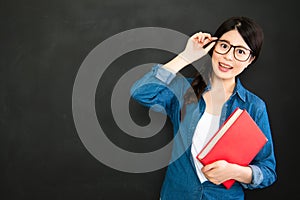 student with glasses and textbook standing in front of blackboard