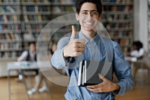 Student guy posing in library showing thumbs up at camera