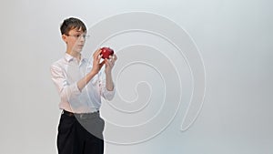 The student guy or schoolboy with glasses looks at a red apple in surprise. A teenager in black trousers, a white shirt with