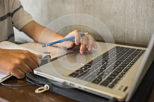 Student hand holding pencil and using laptop touchpad