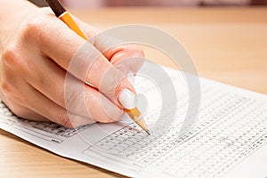 Student hand testing in exercise and passing exam carbon paper computer sheet with pencil in school test room, education concept