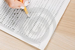 Student hand testing in exercise and passing exam carbon paper computer sheet with pencil in school test room, education concept