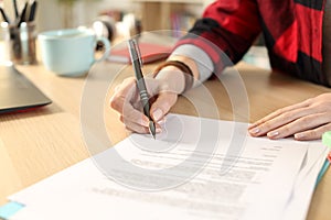 Student hands signing contract sitting at home