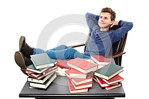 Student having a rest with the legs on the desk, daydreaming among piles of books