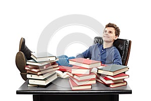 Student having a rest with the legs on the desk, daydreaming among piles of books