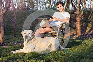 Student with his dog, works from home, in the garden, on a laptop with a helmet