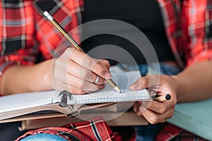 Student holding books and writing in notebook with pencil