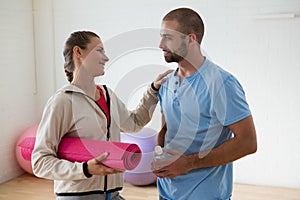 Student holding exercise mat talking to instructor in health club