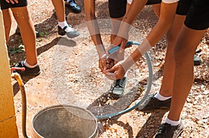 Student holding garden hose spraying fresh water to wash hands