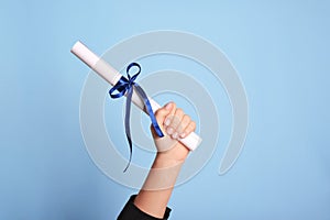 Student holding rolled diploma with ribbon on light blue background, closeup