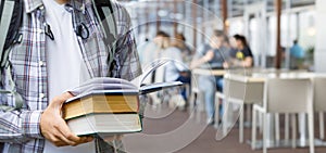Student holding a stack of textbooks in front of a cafe