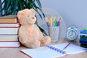 Student home office table with white alarm clock, books, teddy bear, colored notebooks, pencils in glass, chalk board, white alarm