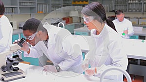 Student in lab coat looking through a microscope