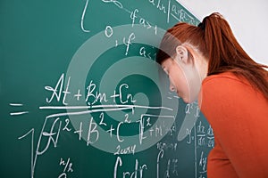 Student leaning head on blackboard in classroom