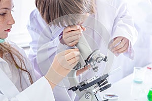 Student learning chemistry. Positive joyful smart boy and girl tesing and using a microscope in science class. Two children help