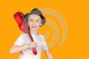 Student learning to play ukuleles. Fashionable boy in summer hat isolated over orange background