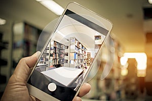 Student Man hand holding mobile smart phone, cellphone over Blur library Book Shelf Natural Background, bokeh out of focus Book