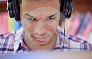 Student, man and online with headphones in library for concentration, studying and learning knowledge for test or exam