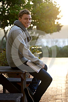 Student, man and outdoor on campus with book in smile, study and prepare for exam with revision notes. Portrait, college