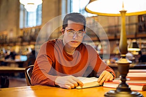 Student man reading book in library wearing eyeglasses