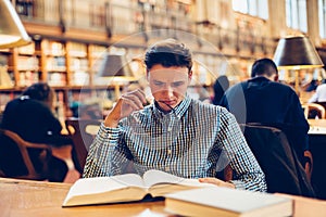 Student man sitting on the desk in library reading room and doing research reading books