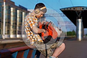 a student poses at a railway station, a boy on the platform is waiting for a train and listening to music with headphones, goes to