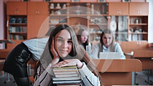 A student poses with textbooks at her desk in her class.