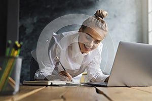 Student preparing for seminar, writing notes in copybook, searching for information online. Female working