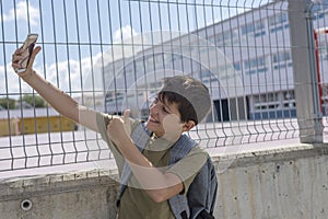 A Student resting outside a school and playing with a mobile phone
