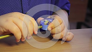 The student's hands sharpen a pencil in a sharpener, close-up.