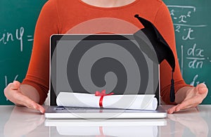 Student showing laptop with mortarboard and degree in classroom