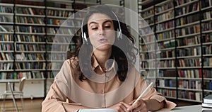 Student sit in library wear headphones talks to online tutor