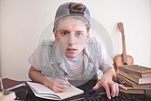 Student sits at a computer near the books, looks at the monitor and writes in a notebook