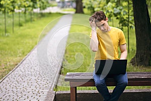 A student sits on a park bench and straightens his hair at a laptop