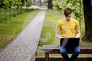 A student sits on a park bench and uses a laptop
