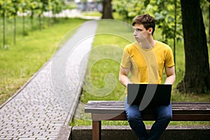 A student sits on a park bench and works using a laptop