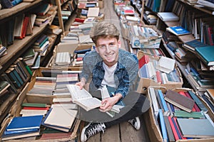 Student sitting with books in his hands on the floor in a public library, smiling and looking at the camera
