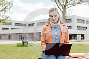 Student sitting on campus of university with her laptop